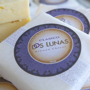This is the image of a piece of cheese wrapped in wax paper with a sticker for Dos Lunas Artisan Cheese