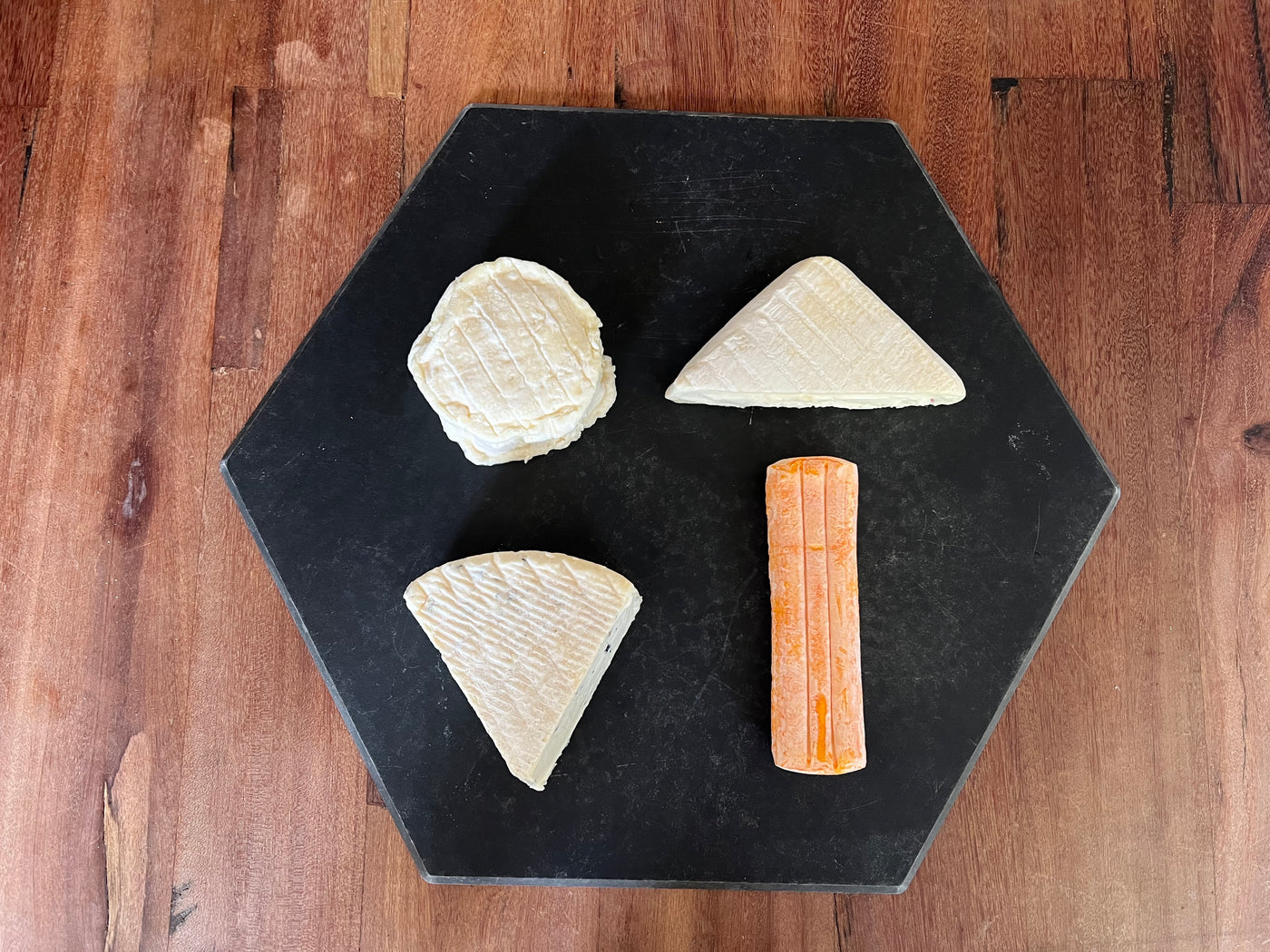 Black cheese board with four different shaped wedges and pieces of soft ripened cheese