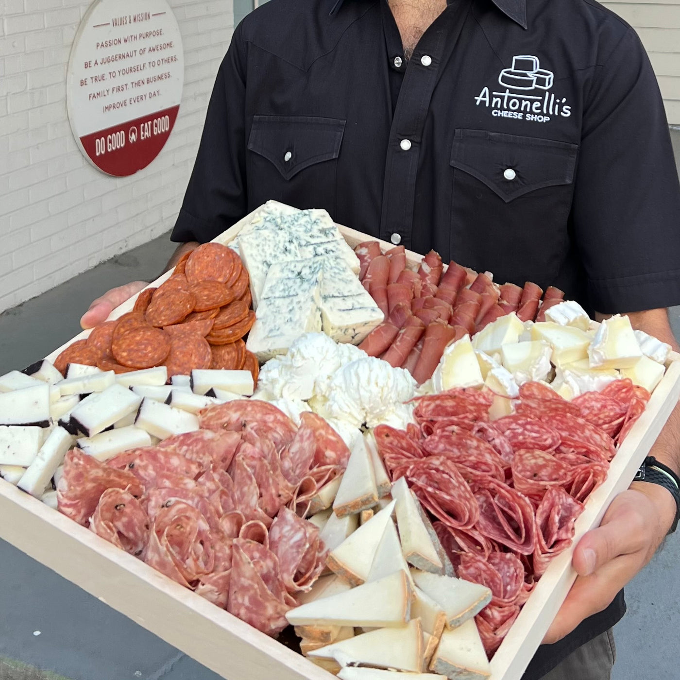 cheesemonger holding a large cheese and meat tray for Thanksgiving Charcuterie Board Ideas