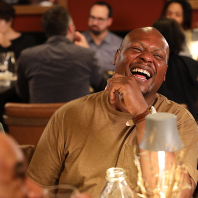 Man laughing heartily at a social gathering with blurred people in the background
