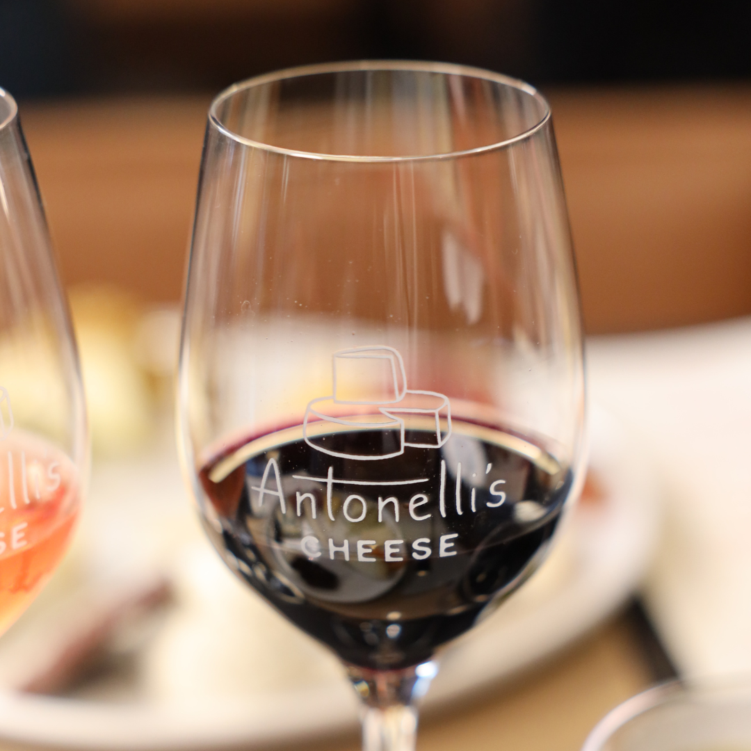 Wine glass with Antonelli's Cheese logo filled with red wine on a blurred background