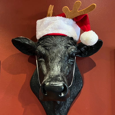 Decorative cow head with Santa hat and reindeer antlers on a red background