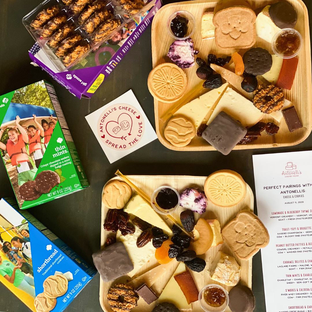 Antonelli's cheese platter with various types of cheese and accompaniments on a black surface, surrounded by packaging and promotional materials.