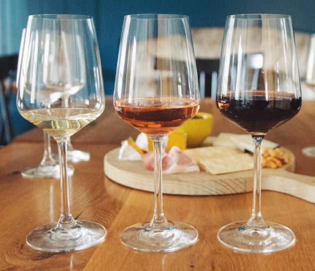 Picture of three wine glasses in the foreground and a cheese plate in the background.