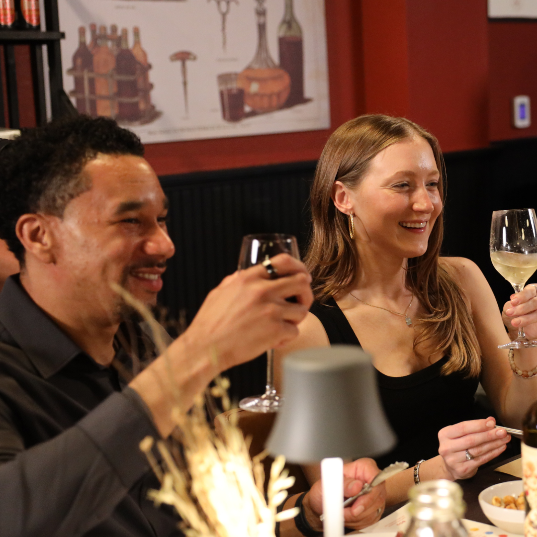 Two people at a dinner table with wine glasses, smiling and enjoying each other's company.