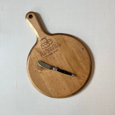 Round cutting board with handle and a black spreader knife resting on it