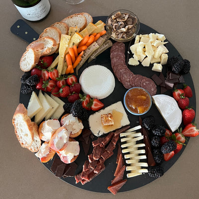 Black round cheese board with a smorgasbord of cheese, meat and pickles