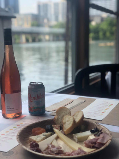 Image of cheese plate, bottle of wine, rambler on a boat