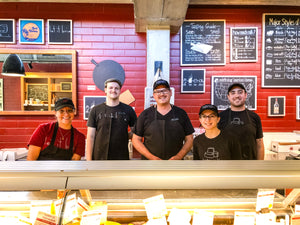 5 cheesemongers standing in the shop behind a cheese case.