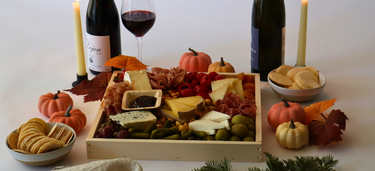 Charcuterie board with cheese, meats, and crackers on a table with pumpkins and candles.