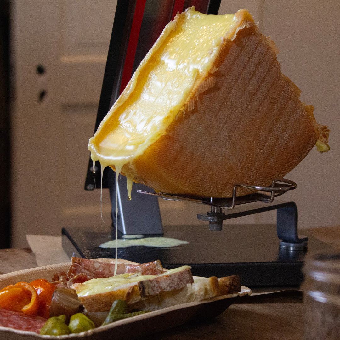 A quarter raclette wheel partially melted and dripping onto bread.  