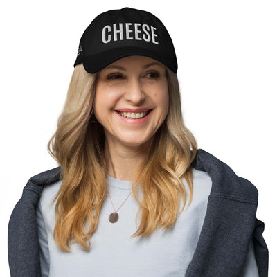 Black "CHEESE" hat with adjustable strap and curved visor worn by a smiling person.