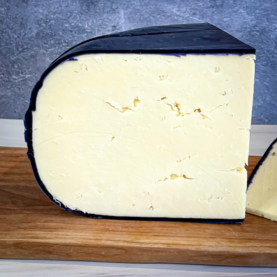 INDIGO RIDGE cheese, aged 8 months, with indigo wax rind on a wooden board.