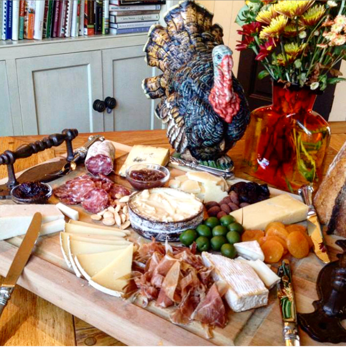 One cheese board with wedges of cheese, sliced meat and pairings with a ceramic turkey decoration for thanksgiving.