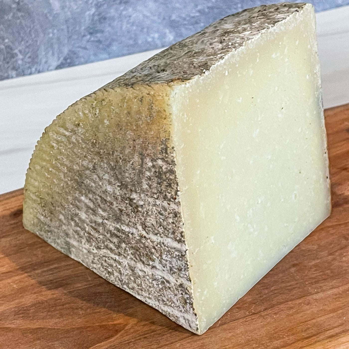1605 Manchego cheese wedge with natural rind on a wooden board.
