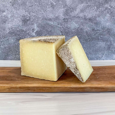 1605 Manchego cheese by Essex St. Cheese on wooden board, featuring a natural rind and rich texture.