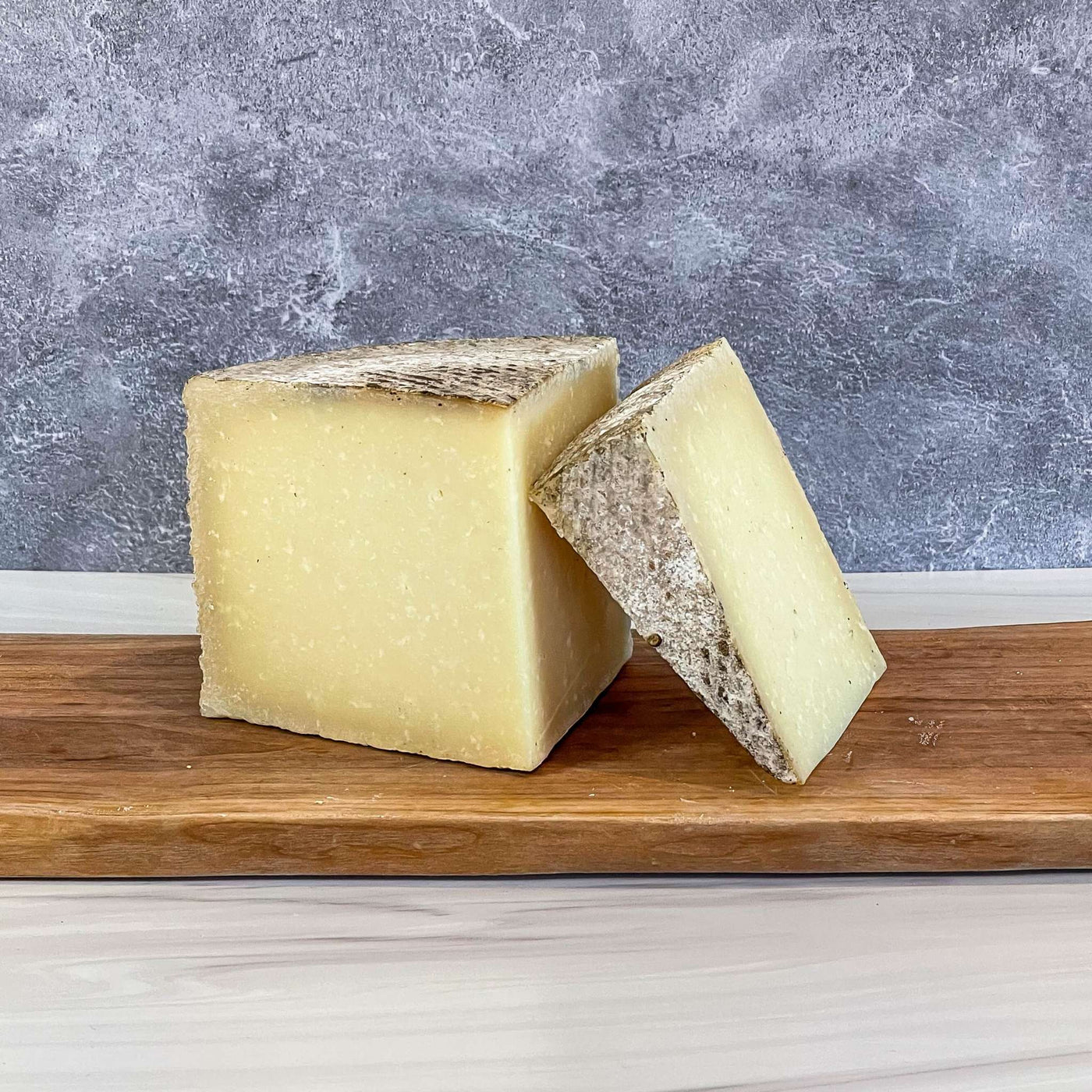 1605 Manchego cheese on wooden board with unwaxed rind, highlighting cross-hatch pattern.