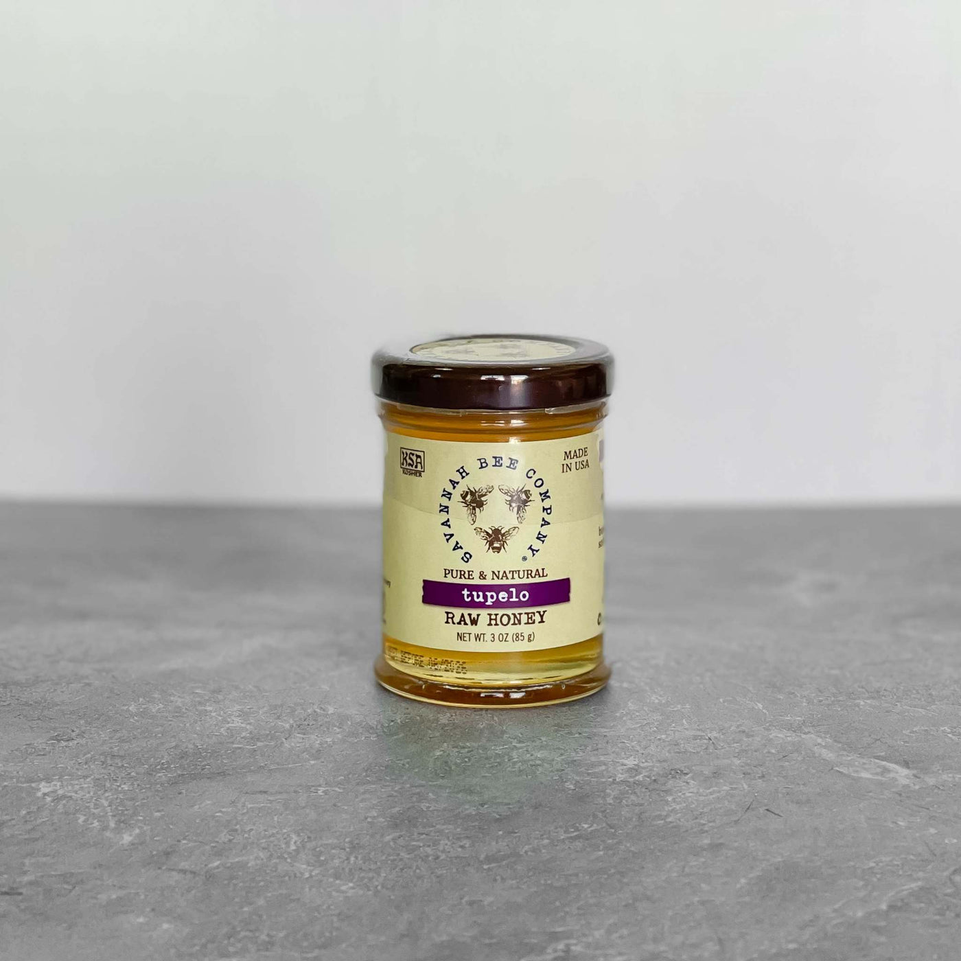 Savannah Bee Company Tupelo Honey jar, 3oz, on a gray surface.