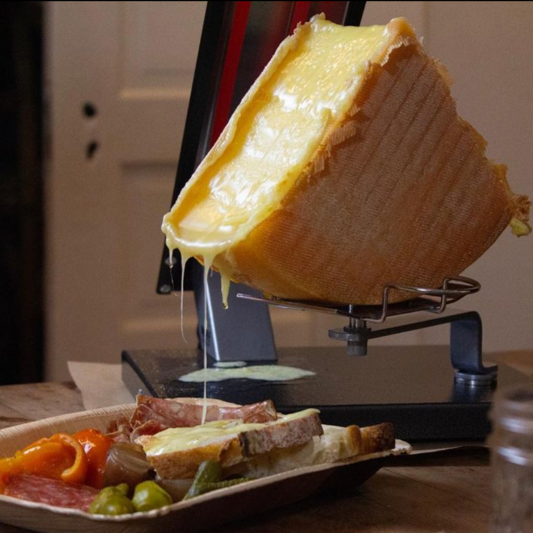 image of melting raclette cheese dripping on a plate of bread and pickles