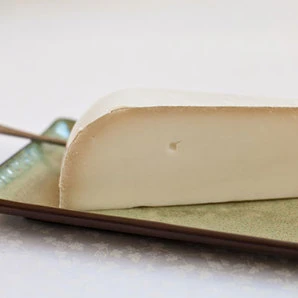 Slice of Brabander Gouda cheese showcasing its smooth texture on a dish.